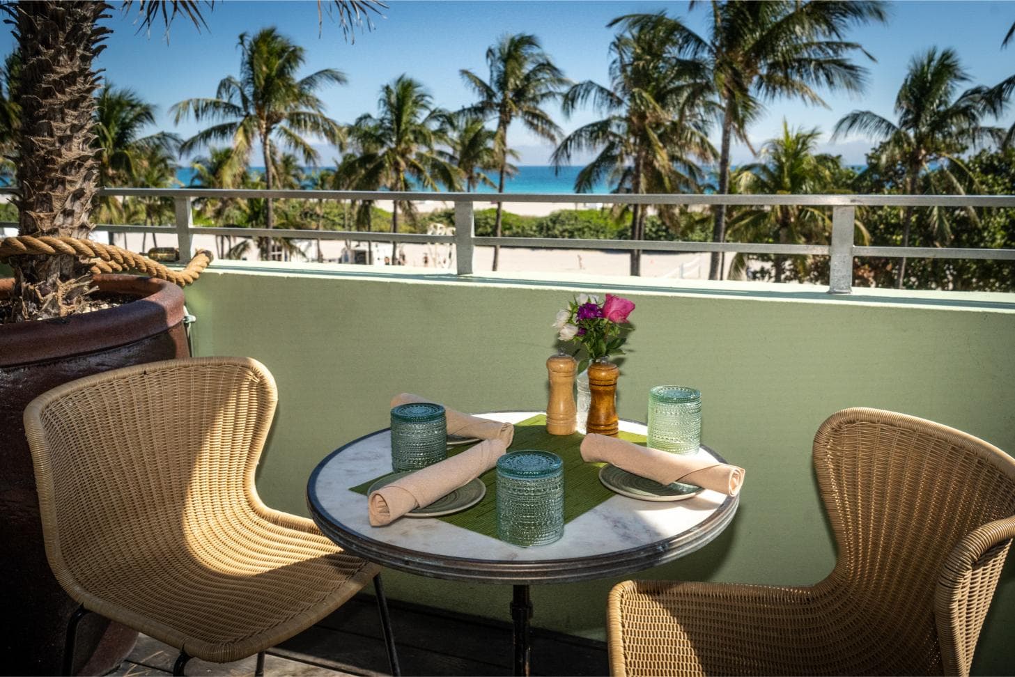 Table for two with flowers on the Pelican Hotel rooftop, overlooking palm trees and the ocean in Miami Beach