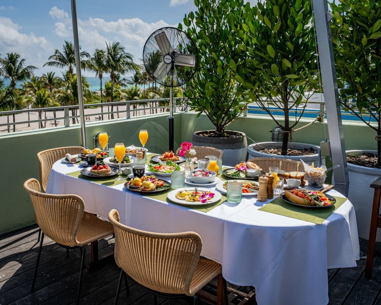 Long table set with brunch dishes and mimosas for a group on the Pelican Hotel rooftop, Miami Beach
